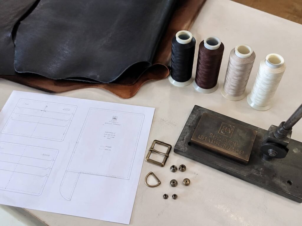 Leather Wallet MOQ: A B2B Guide to Minimum Order Quantities 5 Flat-lay of leather wallet production components — cut leather hide, die-cutting template, thread spools, metal hardware, and a debossing stamp — the inputs that drive leather wallet MOQ